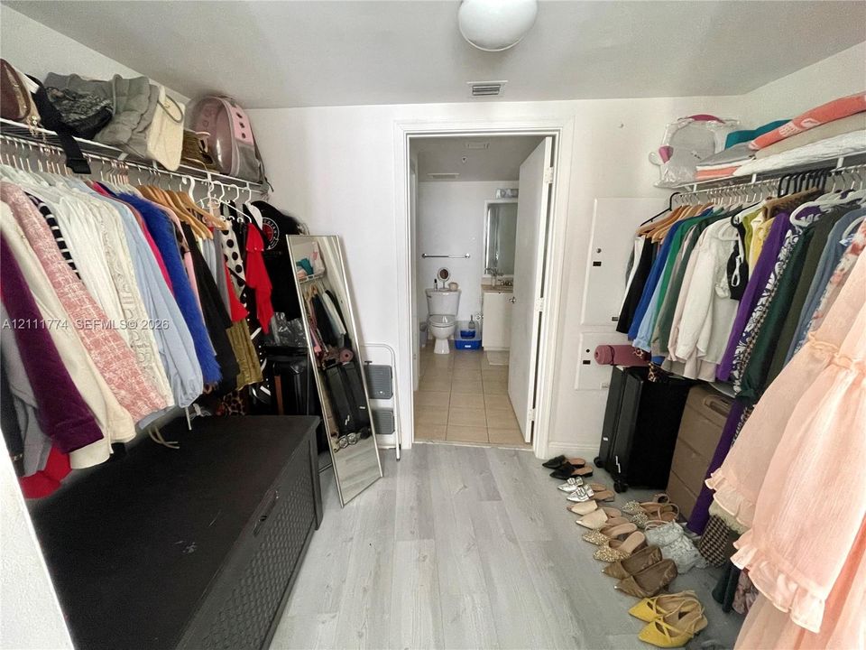 Walk-in closet featuring light-toned wood-finish flooring and dual-sided metal shelving rods