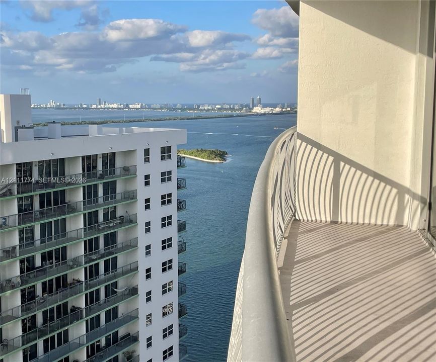 Curved balcony featuring a metal railing and expansive coastal water horizon