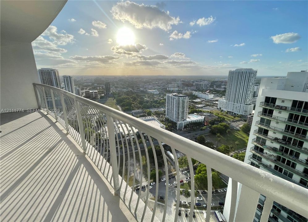 Covered private balcony with a curved metal railing, offering a panoramic outlook over the urban landscape
