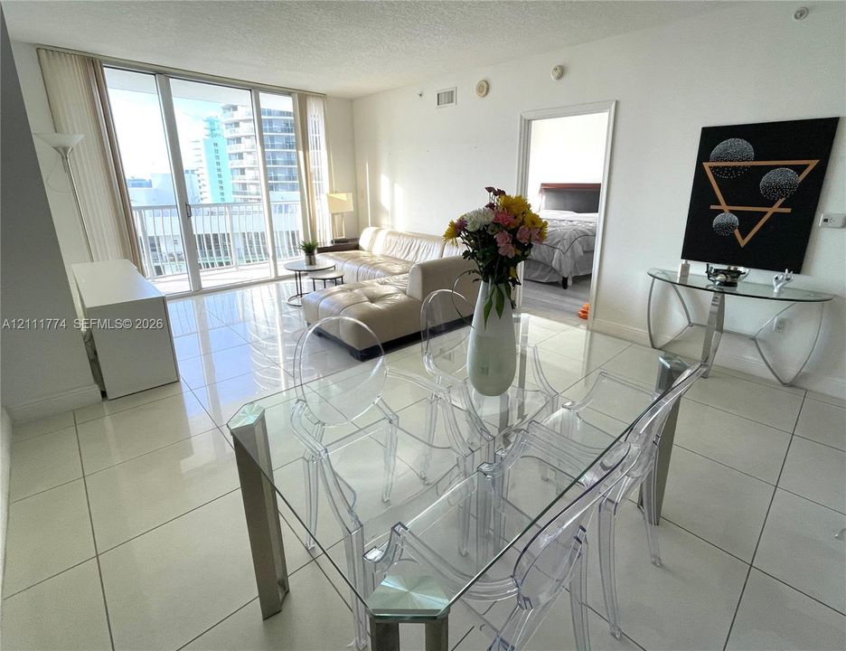 Open-concept living space featuring large-format tile flooring, floor-to-ceiling glass sliding doors, and a private balcony