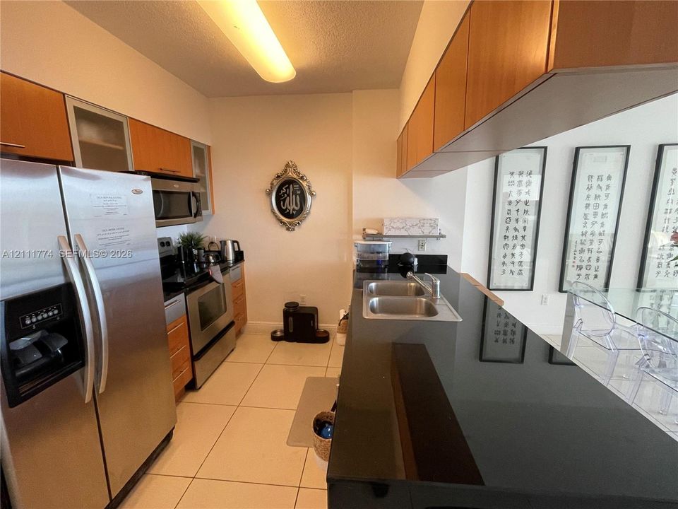 Kitchen featuring flat-panel wood-finish cabinetry, solid surface black countertops, stainless steel appliances, and large-format tile flooring