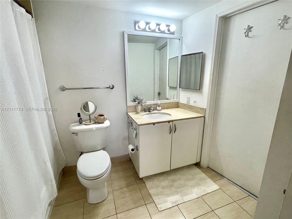 Bathroom featuring a neutral-toned vanity with an integrated basin, a wall-mounted vanity mirror, a multi-bulb light fixture, a porcelain toilet, and tile flooring