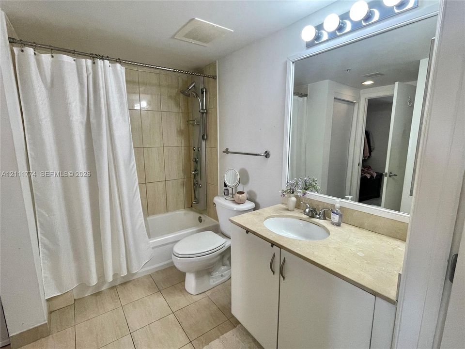 Bathroom featuring a vanity with a neutral-tone countertop, an integrated oval sink, a wall-mounted mirror with integrated lighting, a shower system with a built-in body spray, and tile flooring