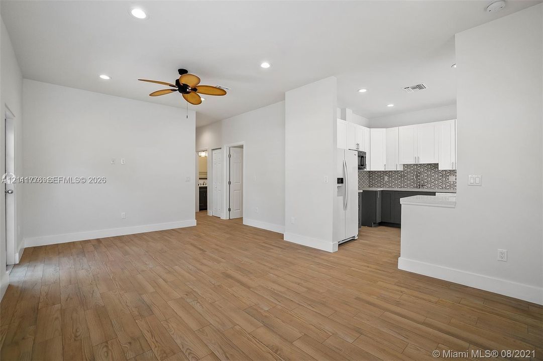 Open-concept floor plan featuring wood-finish flooring, recessed lighting, and a kitchen equipped with white upper cabinetry, dark lower cabinetry, and a geometric-patterned backsplash