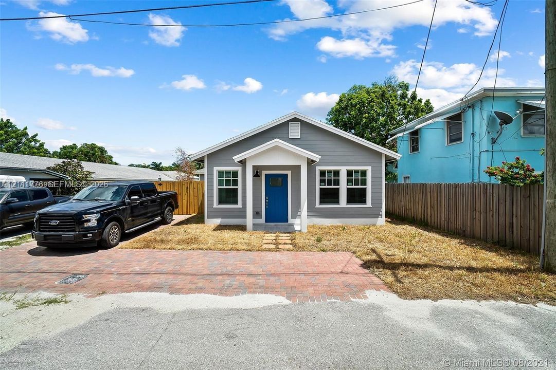 Single-story residence featuring gray horizontal siding, a vibrant blue entry door, a covered porch with white trim, and red brick paved parking