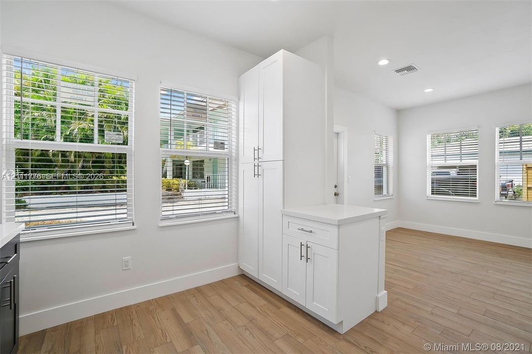Bright room featuring wood-finish flooring, white built-in cabinetry with stone-finish countertops, recessed lighting, and multiple windows with horizontal blinds