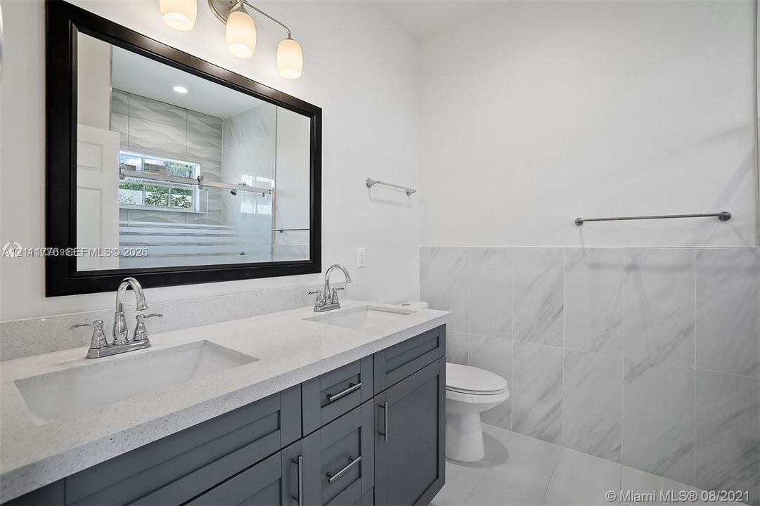 Double vanity featuring a quartz countertop, under-mount sinks, charcoal-toned cabinetry, and large-format tile wainscoting