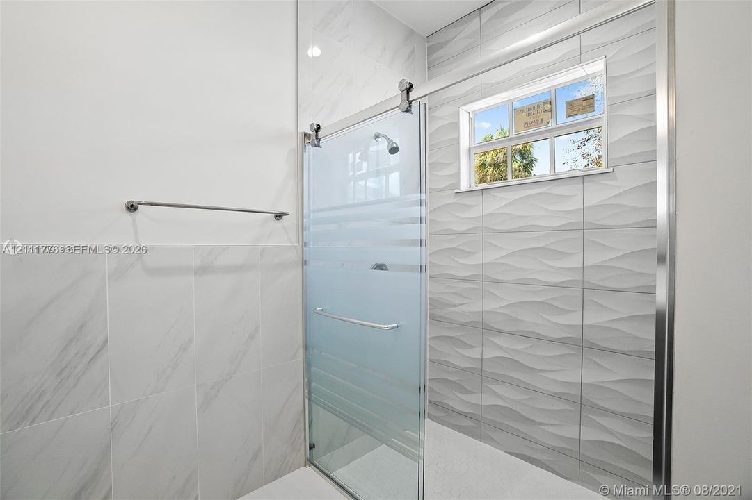 Walk-in shower featuring a sliding frosted glass door, textured wave-patterned tile wall, marble-finish wall tile, and polished metal hardware