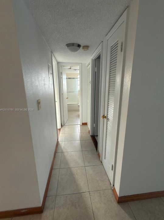 Hallway featuring ceramic tile flooring, neutral wall paint, and closet doors with louvered panels