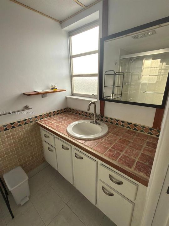Vanity featuring a tiled countertop with decorative trim, an integrated circular sink, polished metal faucet, and white cabinetry