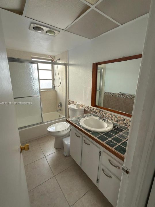 Bathroom featuring a vanity with a tiled countertop, drop-in sink, framed mirror, and a tub-shower combination with a sliding glass enclosure