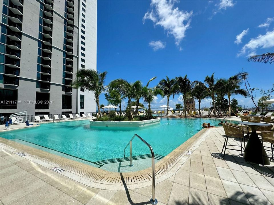 Outdoor swimming pool featuring a central island with palm trees, stone-tile decking, and metal handrails
