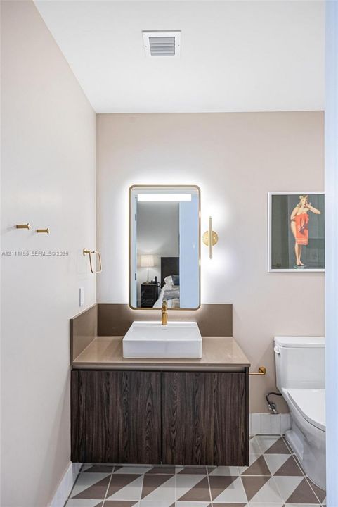 Modern floating vanity featuring wood-finish cabinetry, a white rectangular vessel sink, polished brass hardware, a backlit rectangular mirror, and geometric patterned floor tile