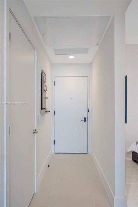 Entry hallway featuring neutral tile flooring, smooth-finish walls, a solid-core entry door with integrated peephole, and recessed ceiling lighting