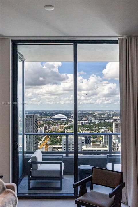 Floor-to-ceiling sliding glass door opening to a private balcony with a metal railing and expansive urban cityscape backdrop
