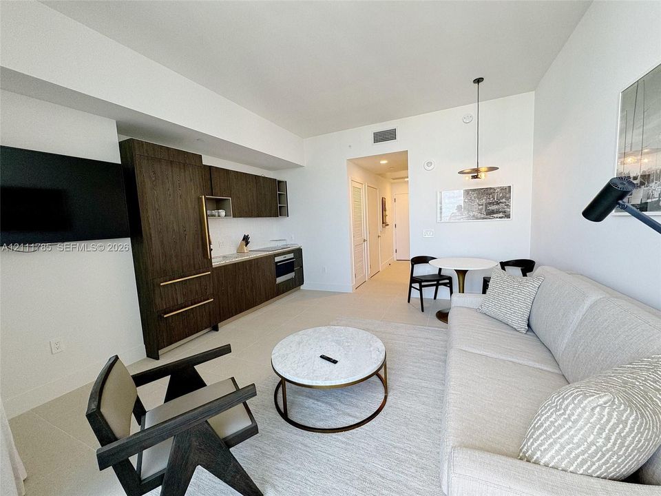 Kitchenette featuring dark wood-finish cabinetry, built-in panel-ready refrigerator, and integrated oven, illuminated by a modern pendant light fixture