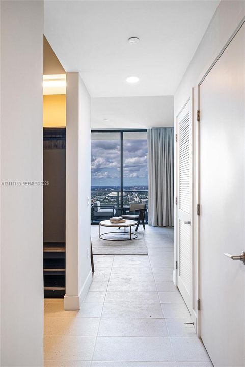 Large-format tile flooring, louvered closet doors, and floor-to-ceiling glass paneling featuring a balcony with an expansive exterior urban landscape