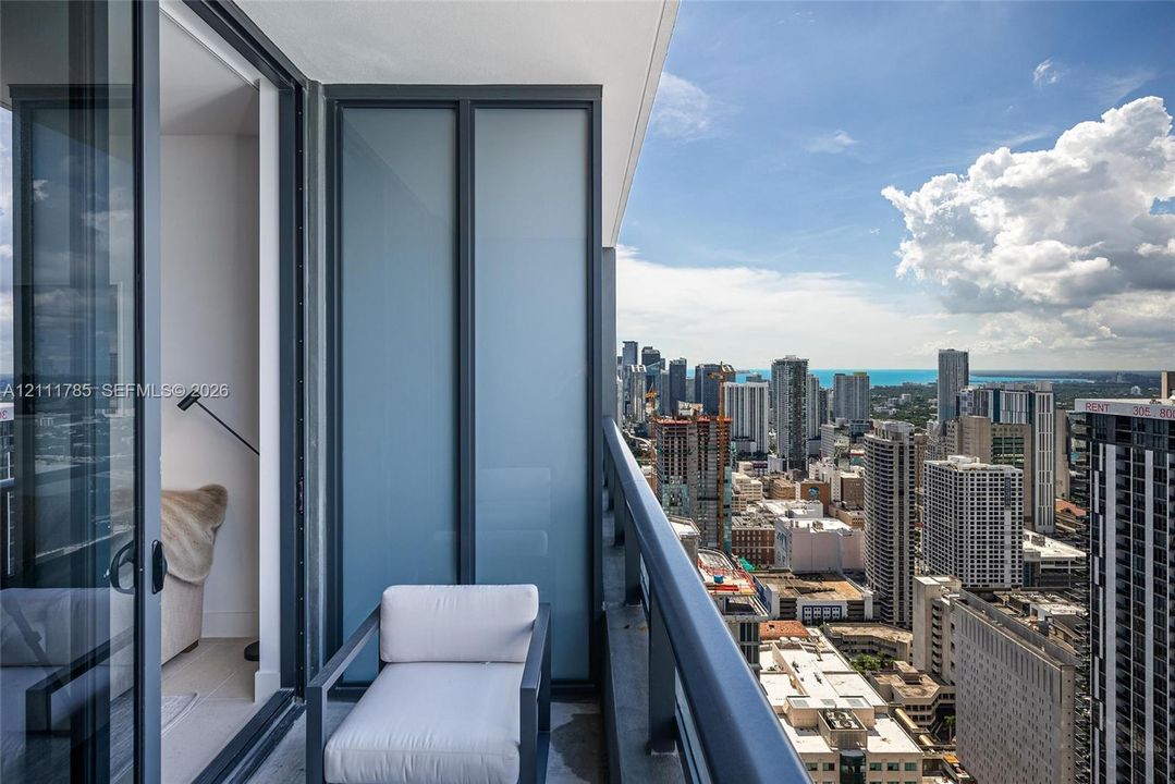 Private balcony featuring floor-to-ceiling glass sliding doors, dark metal railings, and frosted glass privacy panels