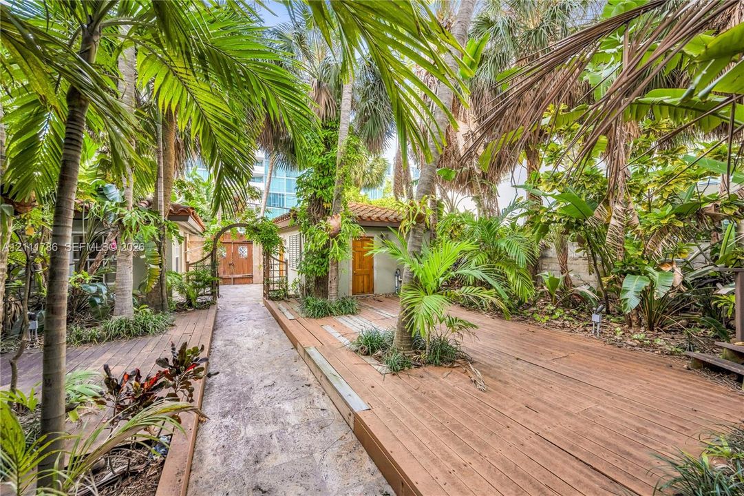 Private outdoor space featuring multi-level wood decking, natural stone pathways, mature palm trees, and an arched garden trellis