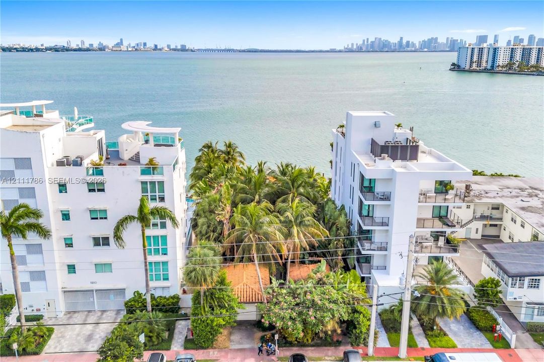 Waterfront property featuring a terra cotta roof, palm tree-lined grounds, and multistory buildings with private balconies