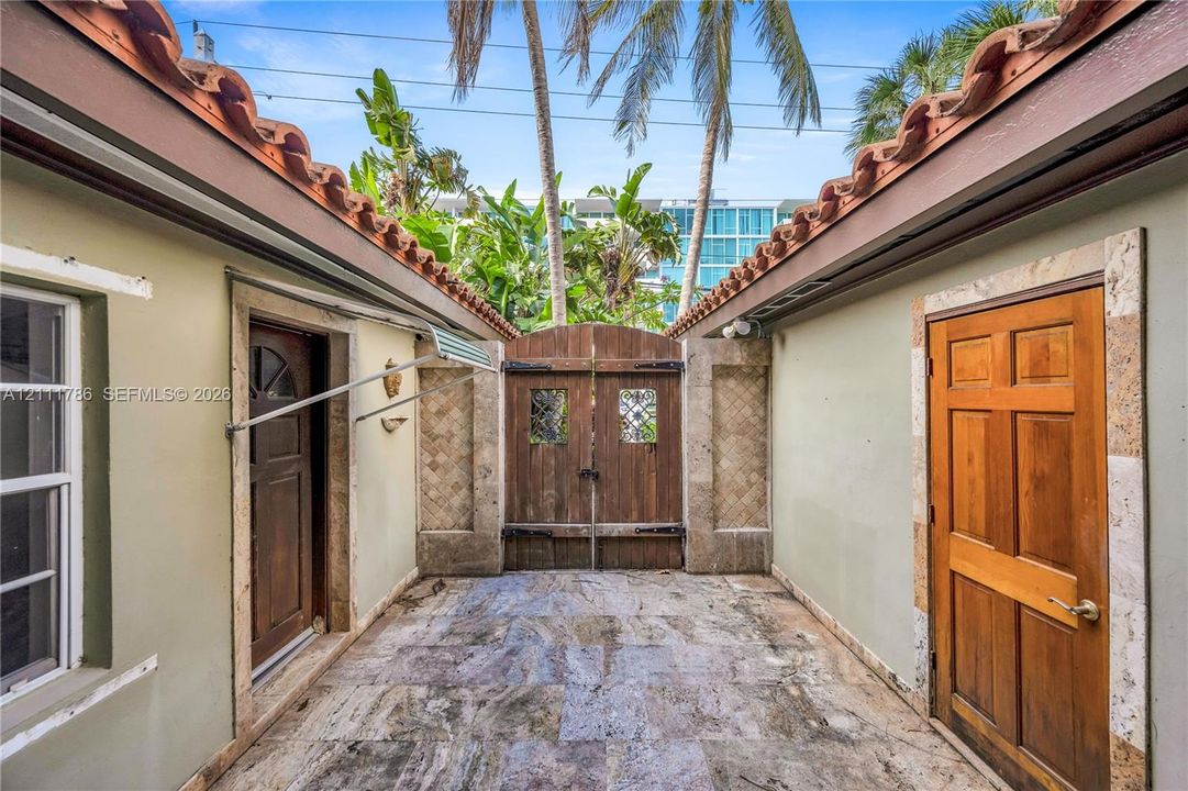 Enclosed courtyard featuring stone tile flooring, two solid wood entry doors, decorative stone door surrounds, and a double-gate wooden entrance framed by a Spanish-style tile roof