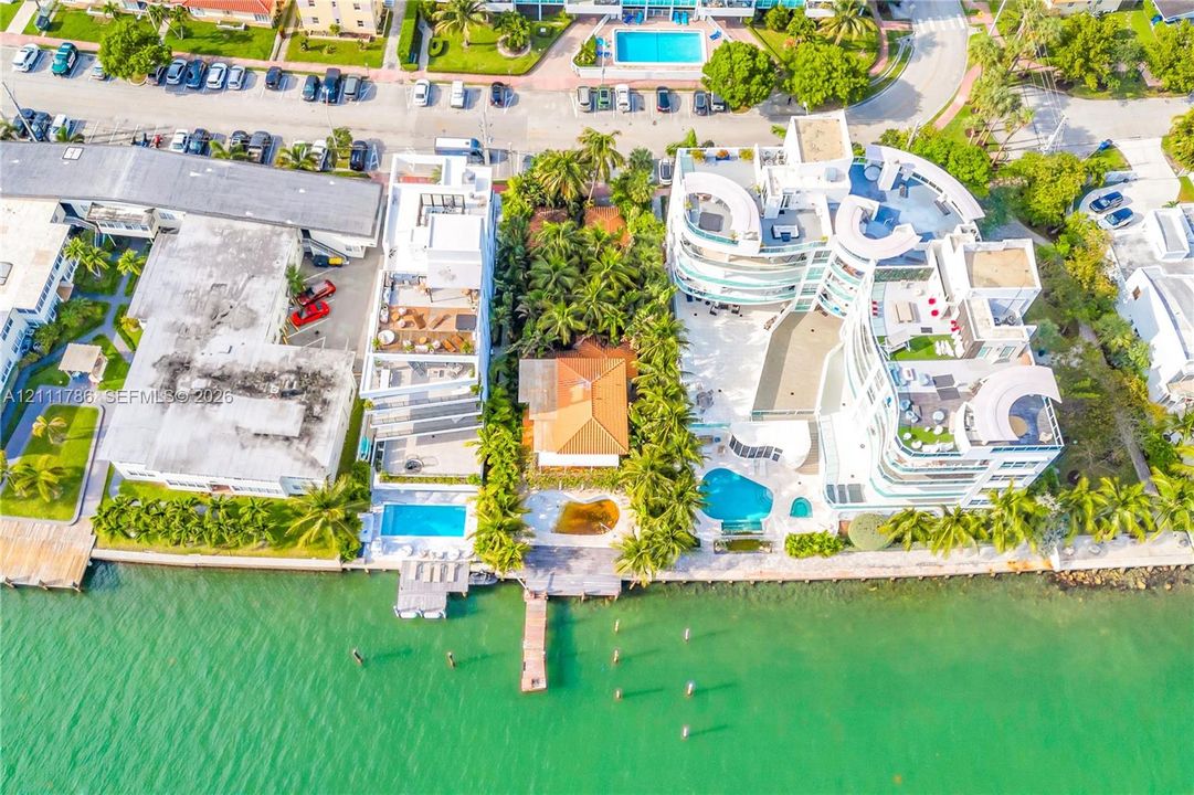 Aerial perspective of waterfront property featuring a tile roof, mature palm trees, a private wooden dock, and bulkhead hardscaping
