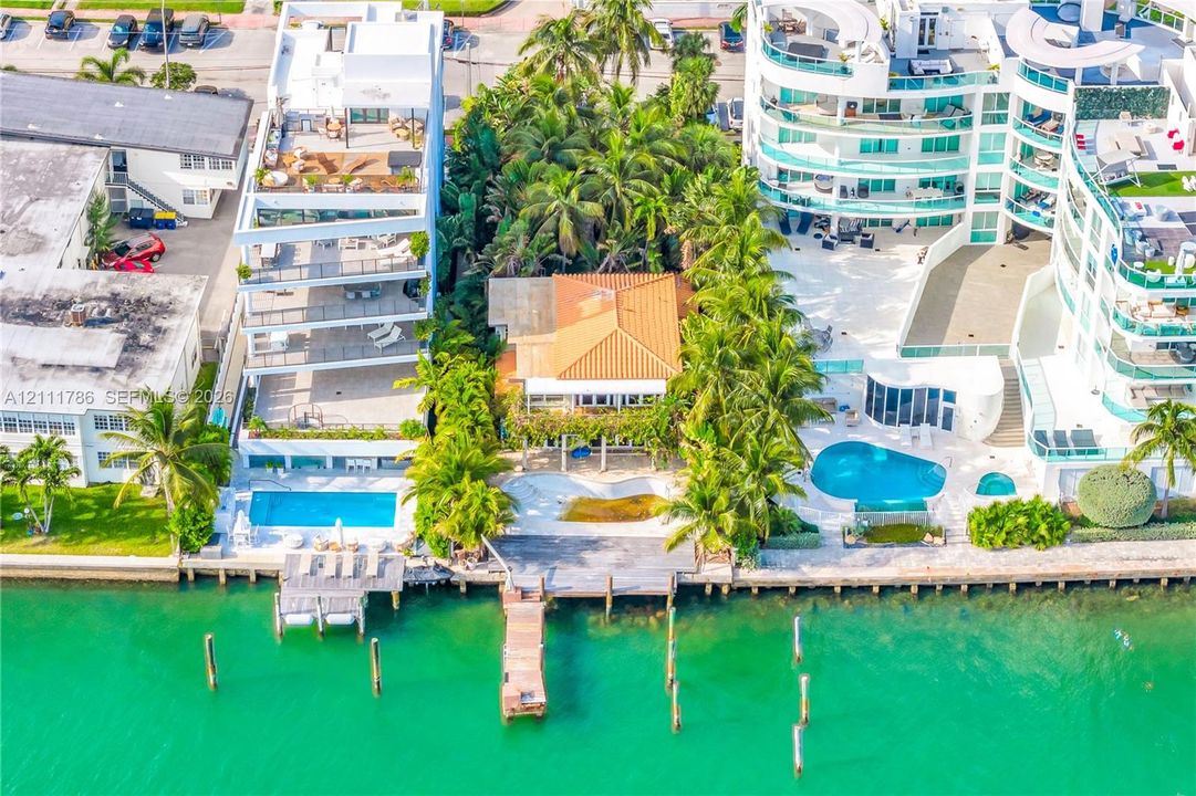 Waterfront property featuring a private wooden dock, clay tile roof, expansive outdoor patio, and mature palm trees