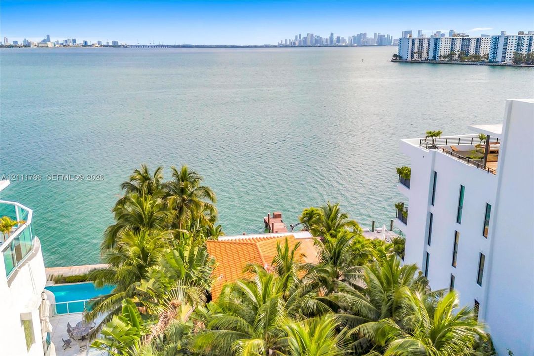 Waterfront property featuring expansive bay exposure, a private swimming pool, mature tropical palms, a terracotta-tiled roof, and a private dock