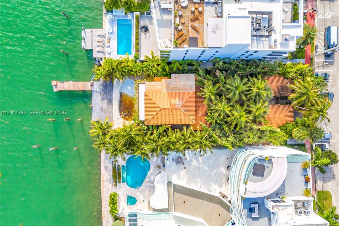 Waterfront property featuring a private dock, clay tile roof, swimming pool, and dense mature landscaping
