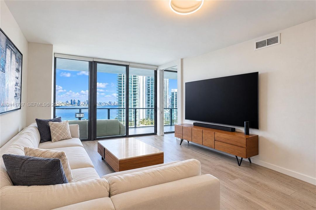 Floor-to-ceiling glass sliding doors, wood-finish flooring, and expansive water and urban skyline scenery