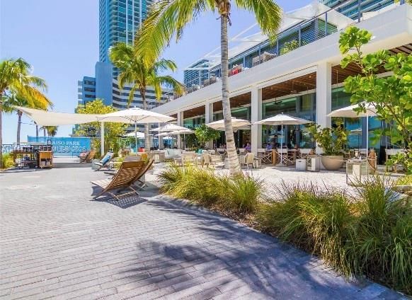 Extensive paved patio area featuring a covered colonnade, native landscaping, mature palm trees, and structural shade sails