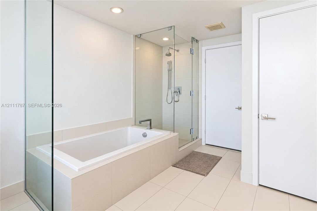 Bathroom featuring a built-in soaking tub with a tiled surround, a glass-enclosed shower, polished chrome fixtures, and large-format tile flooring