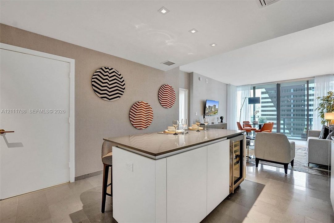 Kitchen island featuring stone countertop, integrated wine refrigerator, minimalist white cabinetry, recessed ceiling lighting, and polished stone flooring