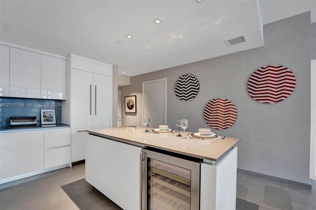 Kitchen featuring flat-panel white cabinetry, a center island with a stone-surface countertop, built-in panel-ready refrigerator, integrated wine cooler, and recessed lighting