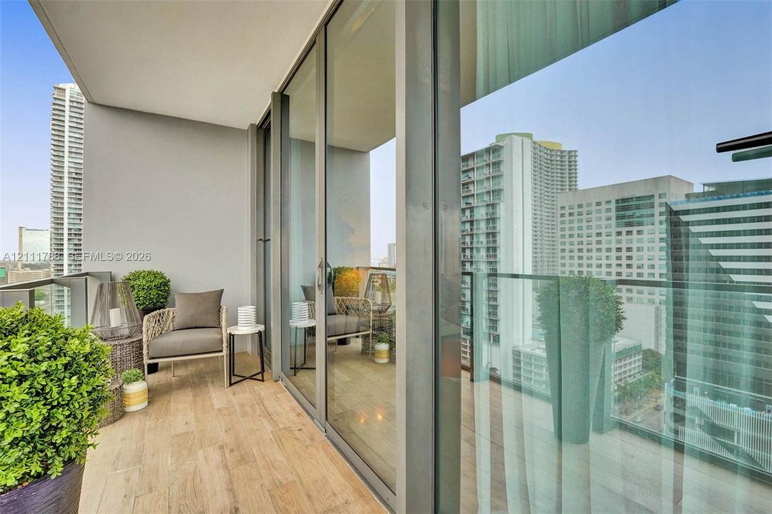 Covered balcony featuring wood-finish flooring, glass panel railings, and full-height sliding glass doors