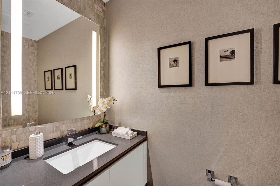 Floating vanity with a smooth solid-surface countertop, integrated rectangular sink, wall-mounted faucet, and floor-to-ceiling mirror with integrated vertical light panels and a tiled backsplash