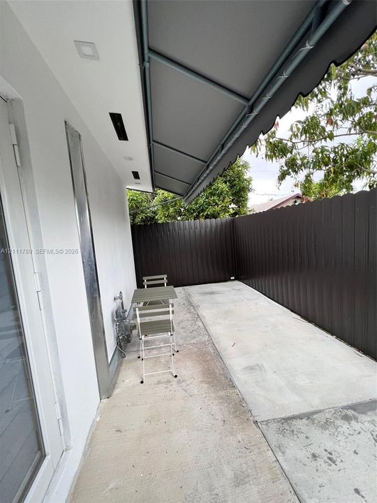 Outdoor patio area featuring a concrete surface, retractable fabric awning, recessed lighting, and a perimeter privacy fence