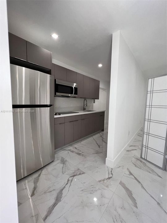 Kitchen featuring matte gray slab-front cabinetry, stainless steel refrigerator, built-in microwave, and large-format porcelain tile flooring
