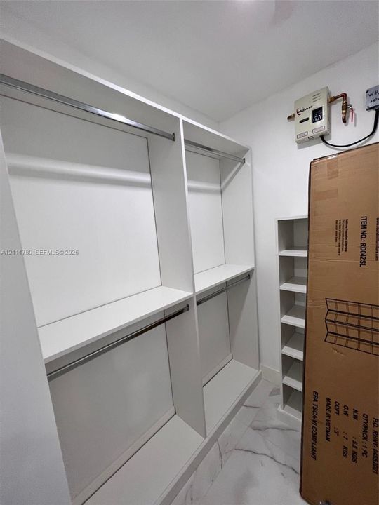 Custom built-in white cabinetry featuring adjustable shelving, multiple metal hanging rods, and stone-finish flooring