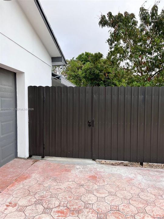 Dark metal scalloped privacy gate featuring a secure lock mechanism, paired with an expansive geometric patterned stamped concrete driveway