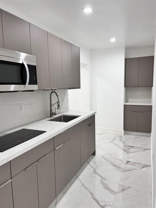 Sleek flat-panel cabinetry, light-toned stone countertops, built-in electric cooktop, stainless steel microwave, and polished tile flooring with marble-finish veining