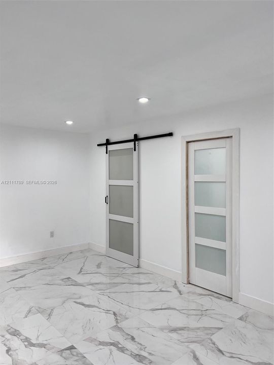 Large-format stone-pattern tile flooring, sliding barn door with matte black hardware, and two frosted glass-panel doors with white trim