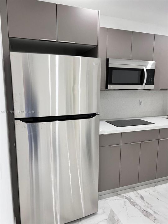 Flat-panel cabinetry in a neutral finish, stainless steel refrigerator, built-in microwave, stone-surface countertop, and stone-finish flooring with veining detail