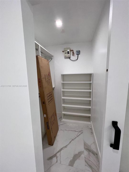 Storage area featuring built-in white shelving, integrated hanging rods, and stone-finish tile flooring