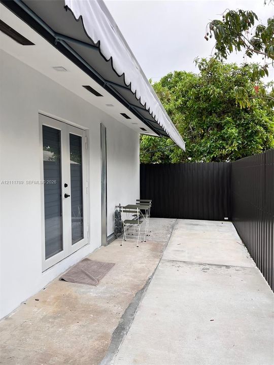 Exterior space featuring concrete patio, retractable awning, glass-panel French doors, and dark metal privacy fencing