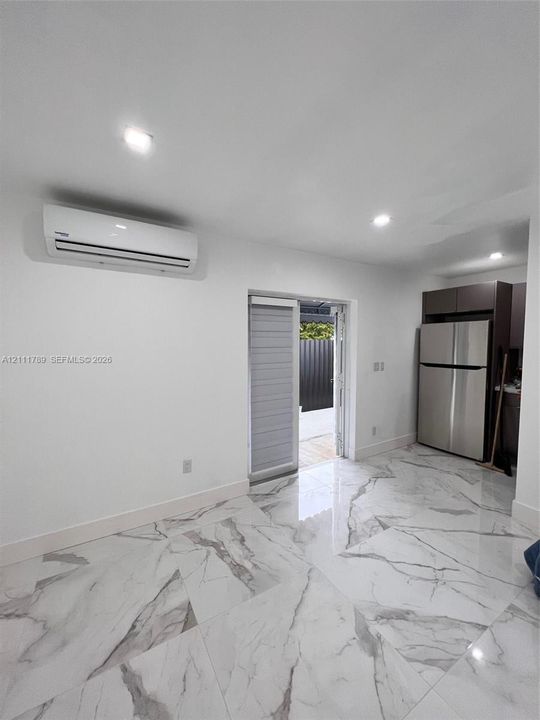 Polished stone-finish flooring, wall-mounted air conditioning unit, stainless steel refrigerator, recessed lighting, and glass-paneled exterior door