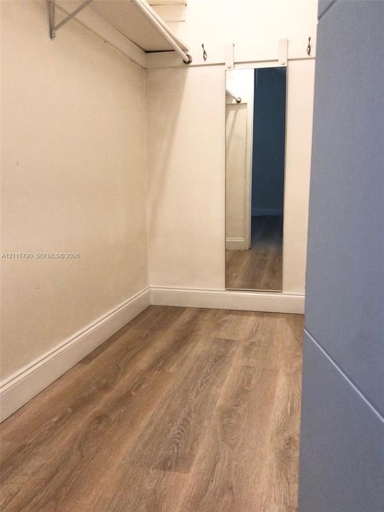 Storage area featuring wood-finish flooring, a wall-mounted full-length mirror, an overhead storage shelf with a hanging rod, and integrated wall hooks