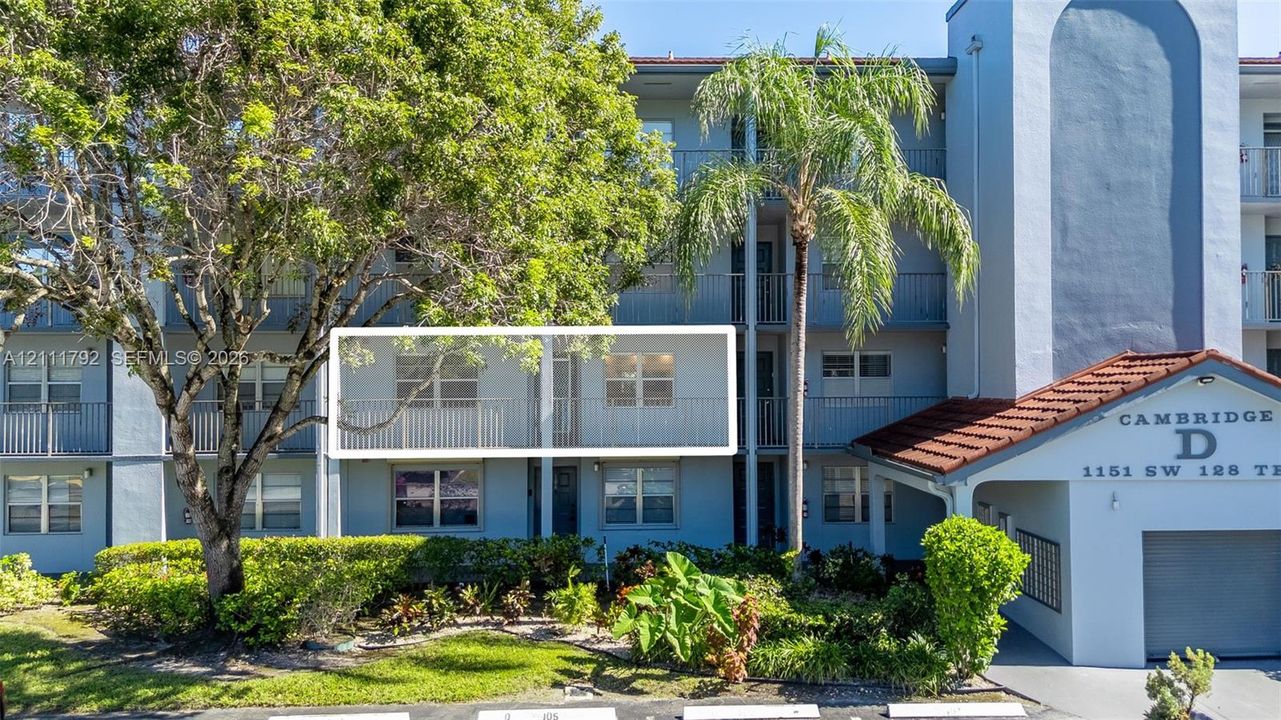 Multi-story building exterior featuring a private balcony, arched architectural detail, clay tile roofing accents, and mature tropical landscaping