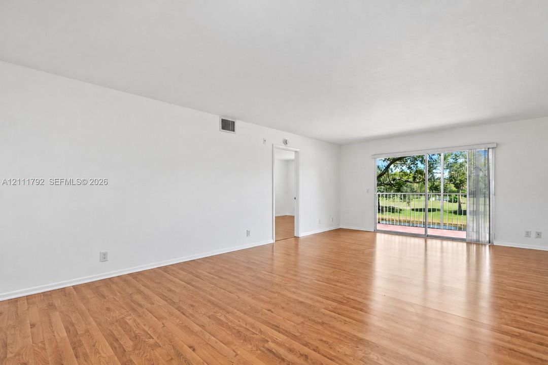 Spacious room featuring wood-finish flooring, neutral wall tones, and glass sliding doors leading to a balcony