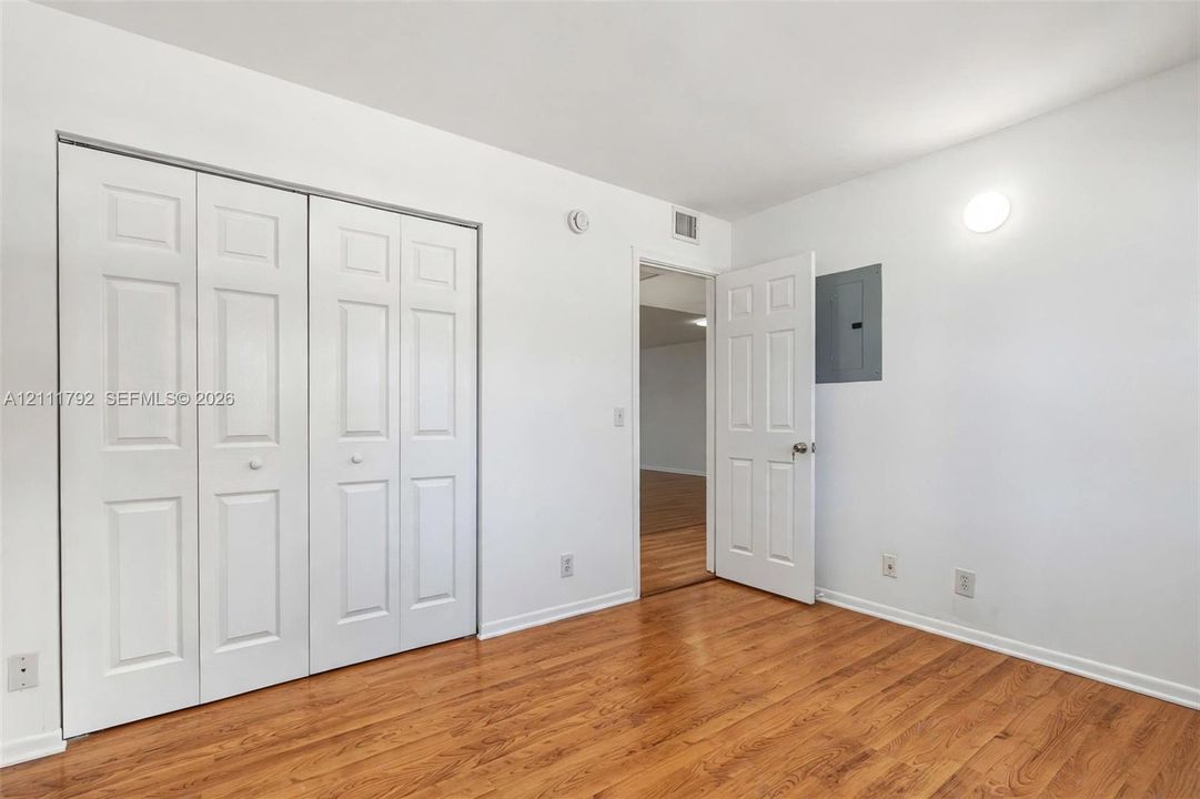 Room featuring wood-finish flooring, white walls, and a large bi-fold closet